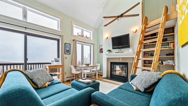 Ein Wohnzimmer mit Türkis-Sofas, einem Kamin, einem Fernseher und einem Balkon mit Blick.