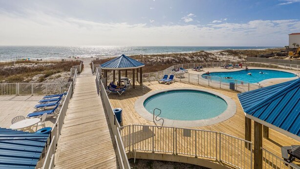 Una terraza de madera con piscina y sillas de descanso con vista a la playa.