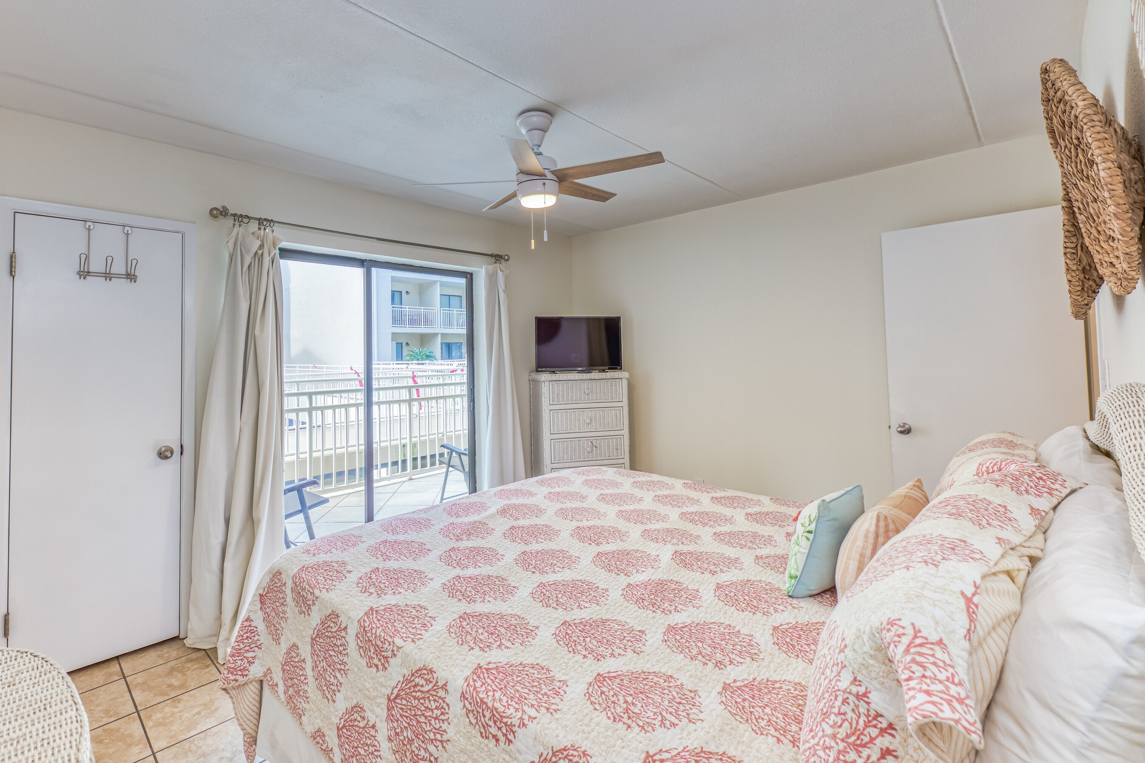 Une chambre avec un lit, un ventilateur de plafond, une télévision et un balcon donnant sur la mer.