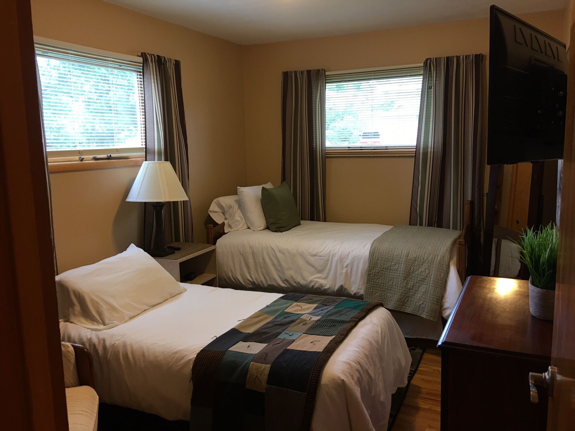 A hotel room with two beds, a desk, a lamp, and a television.