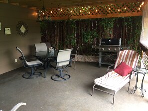 An outdoor patio with a round table, four chairs, a grill, and a lounge chair.