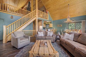 A spacious living area with a wooden staircase, two sofas, a coffee table, and a chandelier.
