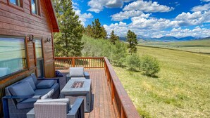 A wooden deck with outdoor furniture, including a sofa and chairs, overlooking a grassy landscape with trees and mountains. - Trout Fishing & Panoramic Views - Starlink, 4BR, Pet-Friendly (Fairplay)