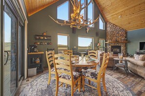 A spacious living room with a large dining table, wooden chairs, a fireplace, and a stone wall.