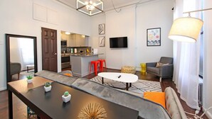 Una sala de estar moderna con comedor, cocina y televisor montado en la pared.