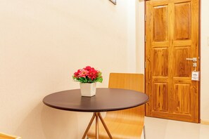 A round table with a white vase containing red flowers, positioned in front of a wooden door with a handle and a lock. - Tree Place by Zuzu (Bangkok)