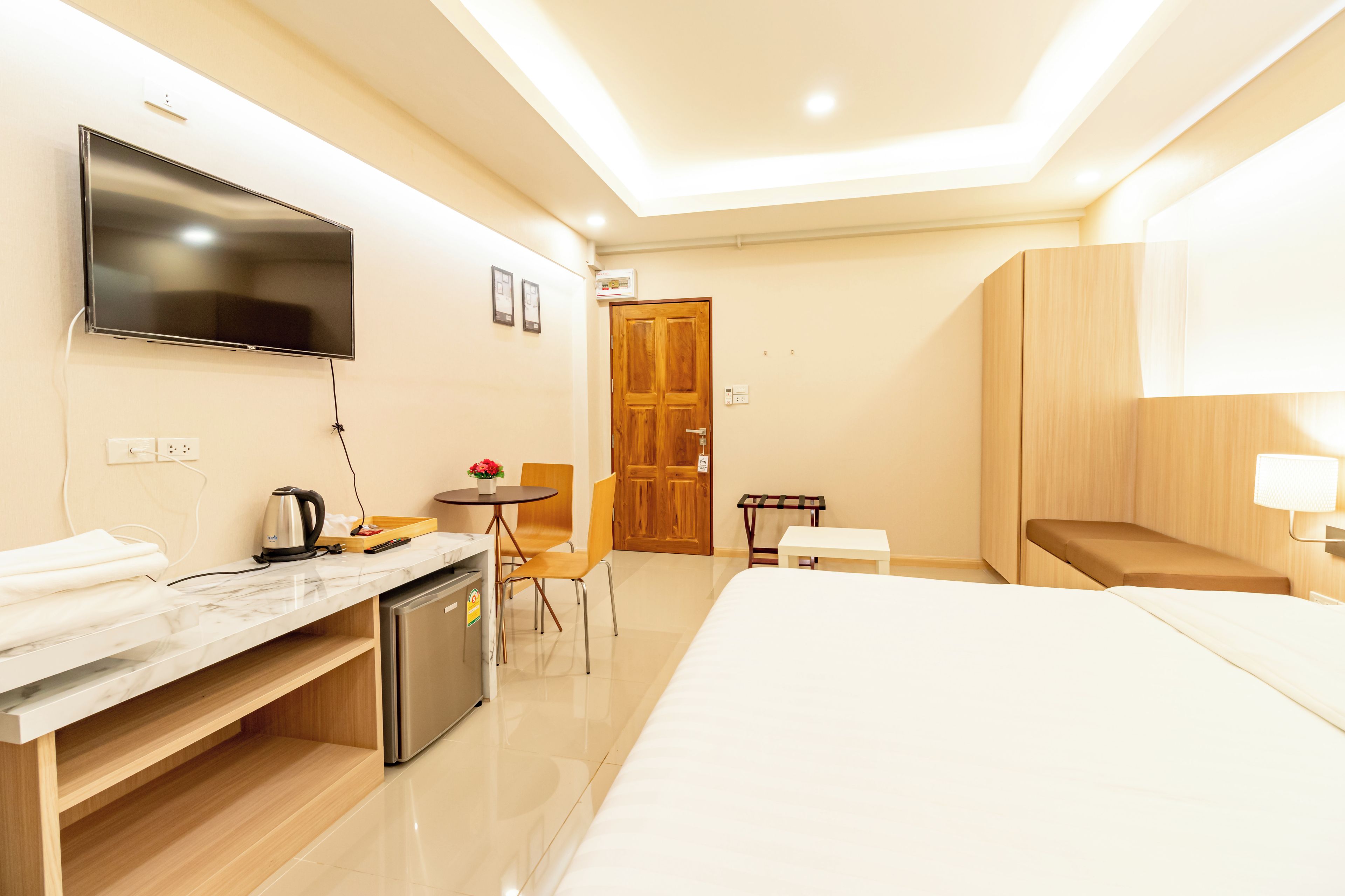 Una habitación de hotel con una cama, un escritorio con hervidor, televisión y puerta de madera.
