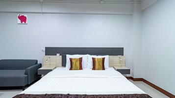 Habitación de hotel con una cama grande, dos mesitas de noche, un sofá gris y una decoración de elefante colgada en la pared.