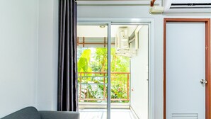 A room with a grey sofa, a sliding glass door leading to a balcony with a view of greenery and a red railing. - Tree Place by Zuzu (Bangkok)