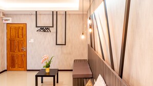 A modern lobby with a wooden door, a black table with a vase of flowers, a bench, and a wall-mounted light fixture. - Tree Place by Zuzu (Bangkok)