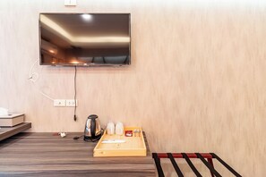 Une chambre d’hôtel dotée d’un téléviseur à écran plat fixé au mur, d’un plateau en bois avec des sachets de thé et une bouilloire, ainsi que d’un banc rouge.