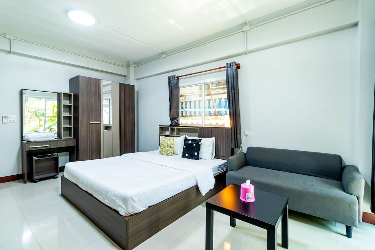 A modern hotel room with a bed, a sofa, a small table, and a window with curtains.
