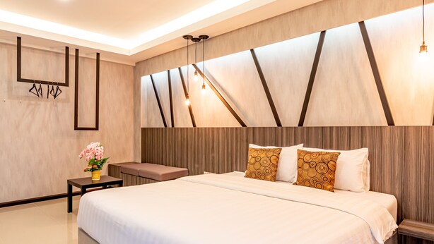 A modern hotel room with a large bed, a bedside table with a vase of flowers, and a wall-mounted light fixture. - Tree Place by Zuzu (Bangkok)