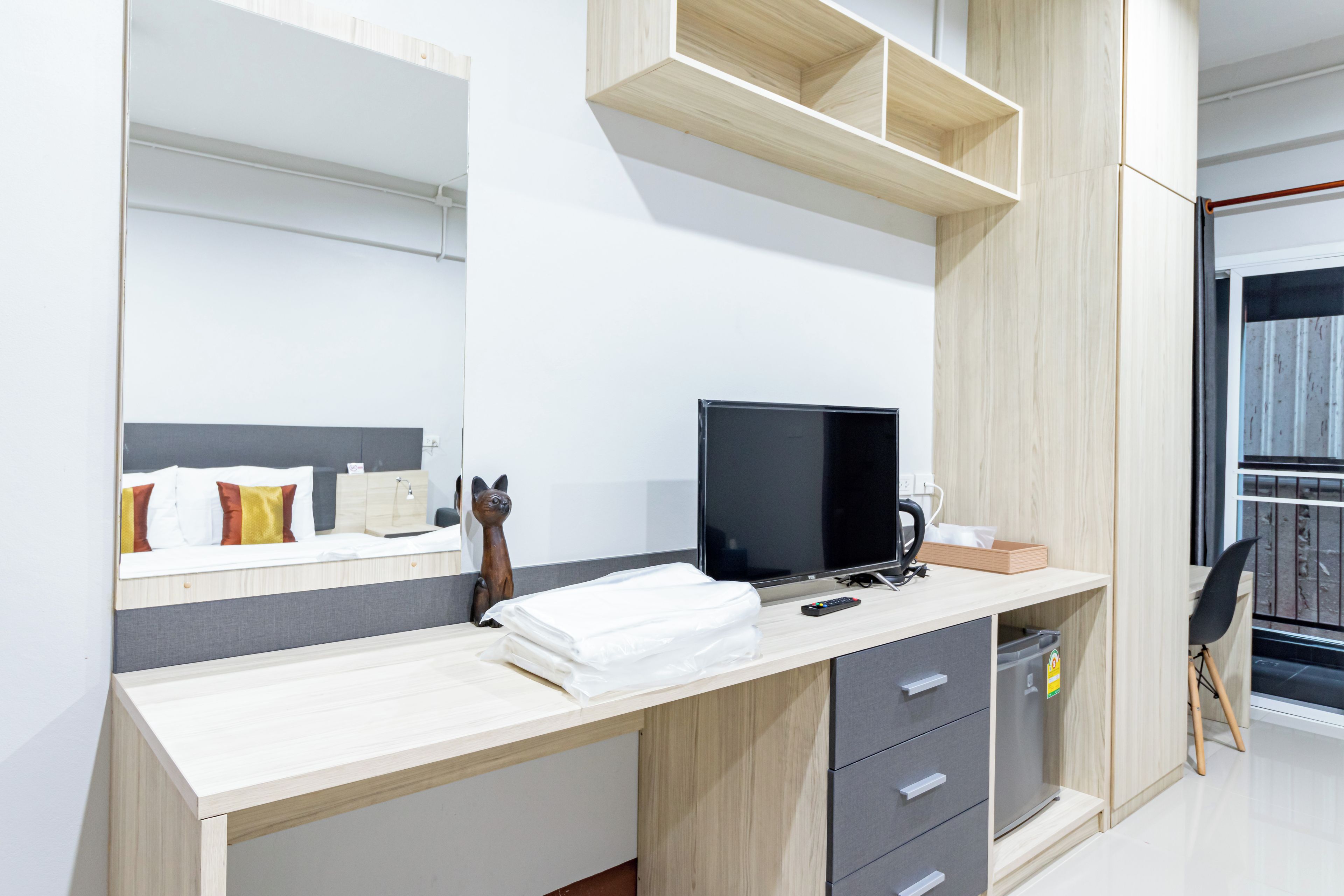 A modern hotel room with a wooden desk, a flat-screen TV, a cat figurine, and a large mirror.