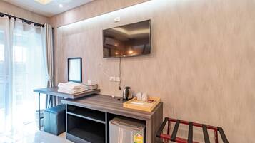 A modern hotel room with a flat-screen TV mounted on the wall, a small kitchenette with a refrigerator, and a seating area with a chair and a table.