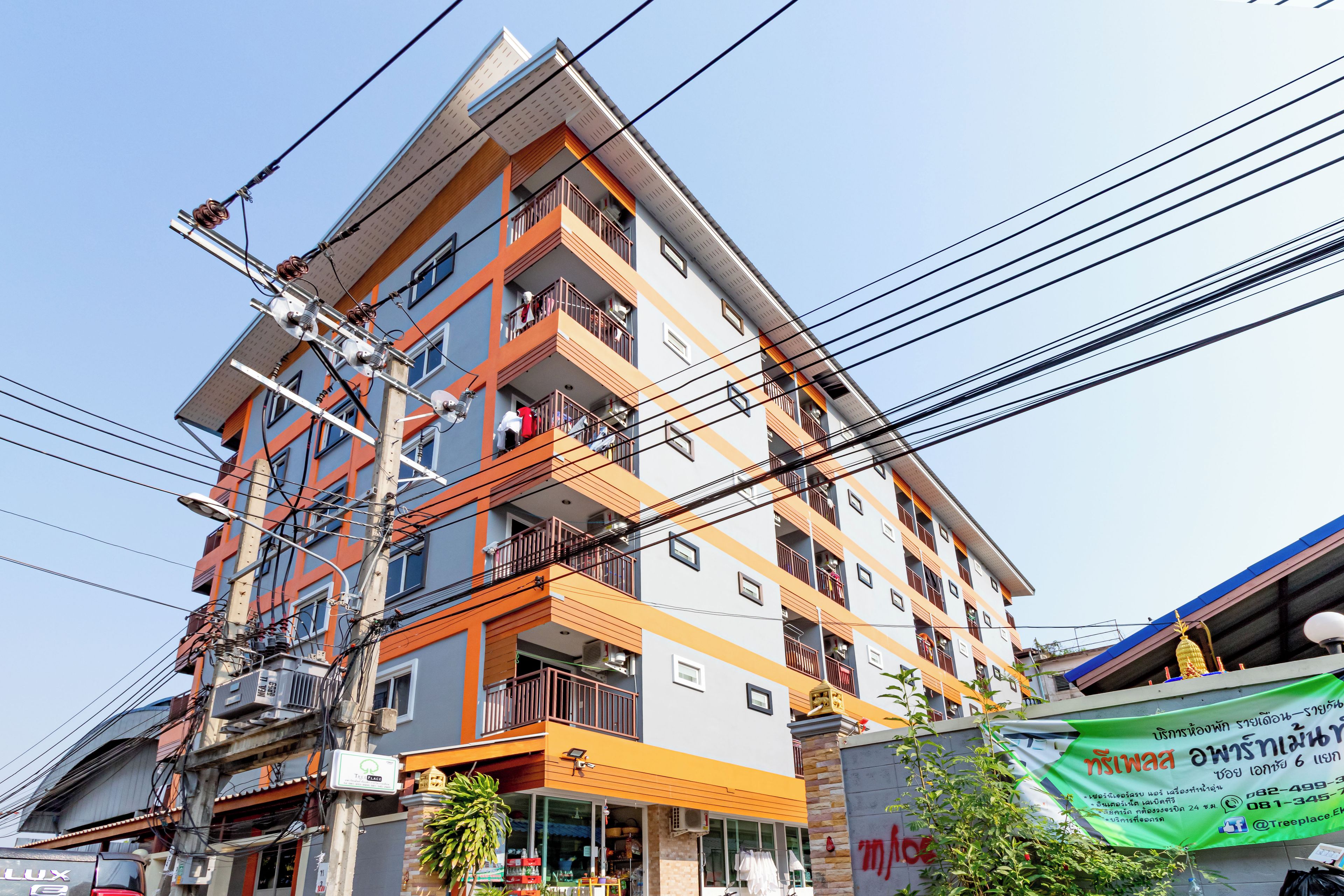 Un edificio de varios pisos con balcones, una tienda en la planta baja e infraestructura eléctrica visible.