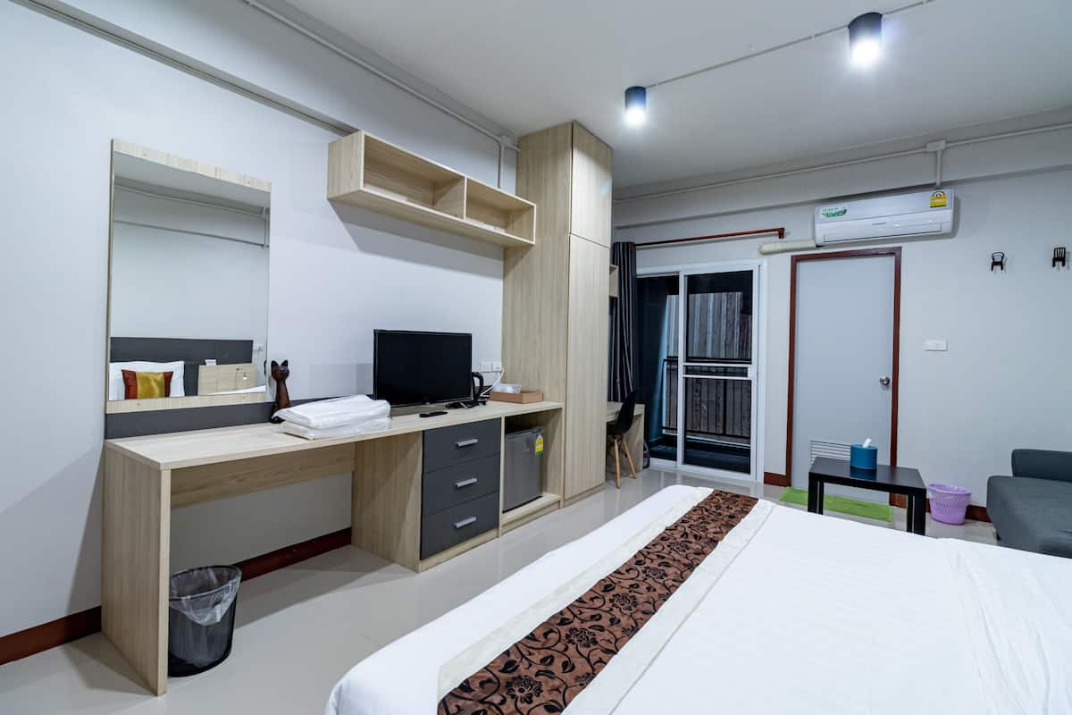A modern hotel room with a wooden desk, a bed with a patterned bedspread, a TV, a wardrobe, and an air conditioning unit.