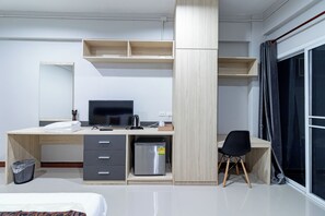 A modern hotel room with a wooden desk, a bed, a small refrigerator, and a large window with curtains. - Tree Place by Zuzu (Bangkok)