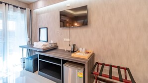 A modern hotel room with a flat-screen TV mounted on the wall, a small table with a kettle and a tray, a mini-fridge, and a red chair. - Tree Place by Zuzu (Bangkok)
