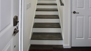 Een trap met witte muren en donkere houten treden die uitkomen op een plateau.
