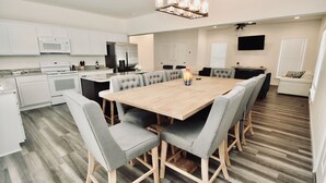 Een moderne keuken met witte kasten, een magnetron, en een eethoek met een houten tafel en stoffeerde grijze stoelen.