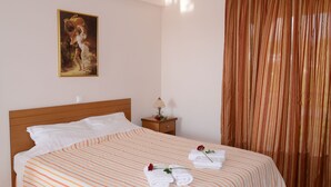 A neatly made bed with striped bedding, a nightstand with a lamp, and a painting on the wall. - Studio for 2 Guests (Nafplio)