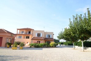 A two-story building with a tiled roof, a balcony, and a gravel driveway.