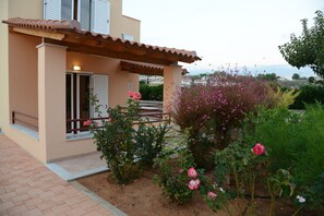A house with a tiled roof, a wooden pergola, and a garden with pink flowers.