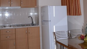 A kitchen with wooden cabinets, a white refrigerator, and a dining table with chairs. - Studio - Apartment for 3 Guests (Nafplio)