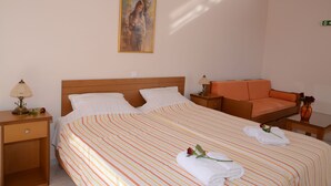 A hotel room with a bed, a nightstand, a chair, a table, and a painting on the wall. - Studio - Apartment for 3 Guests (Nafplio)