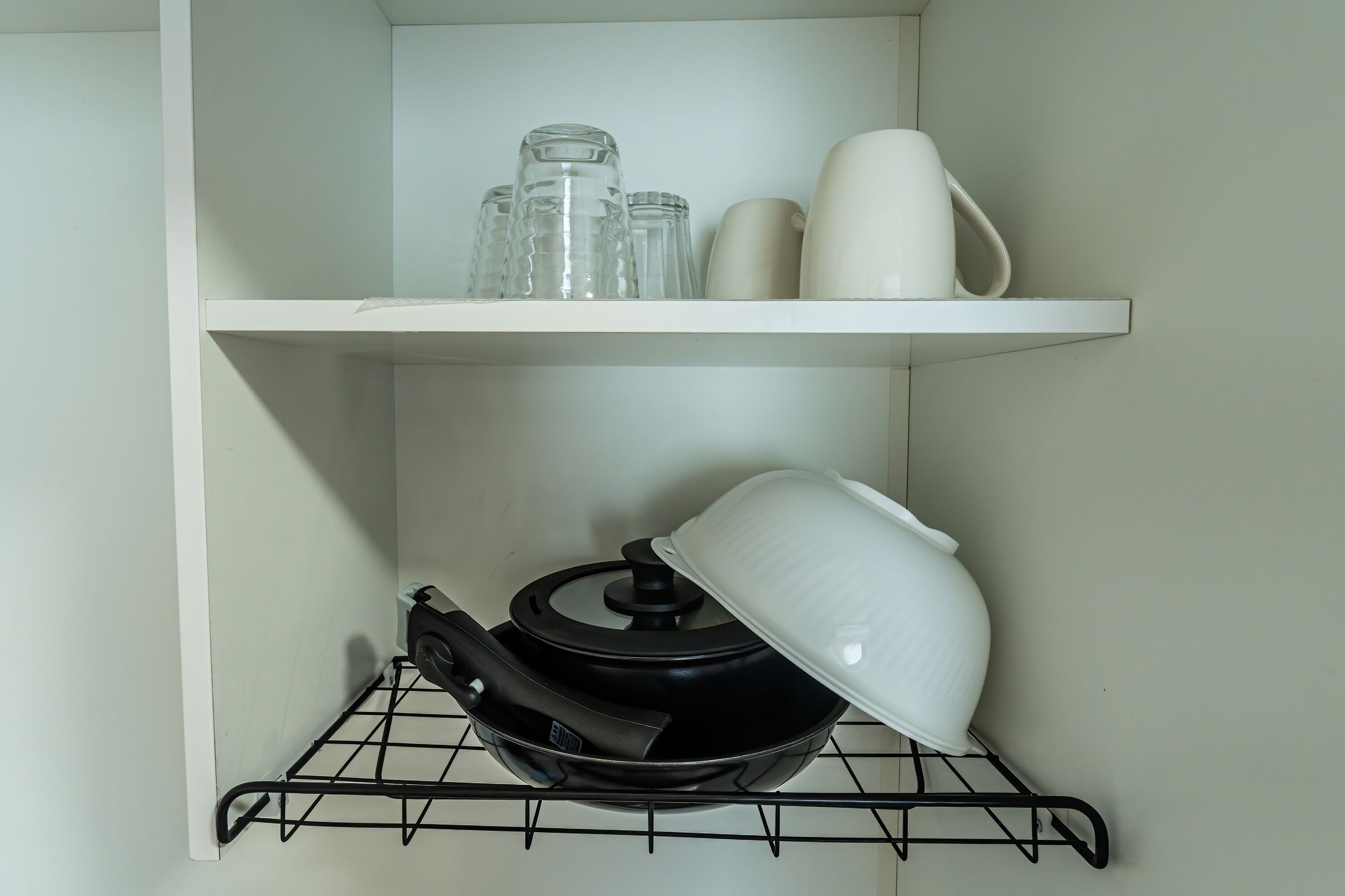 A kitchen shelf with a black frying pan, a white pot, and a white pitcher.