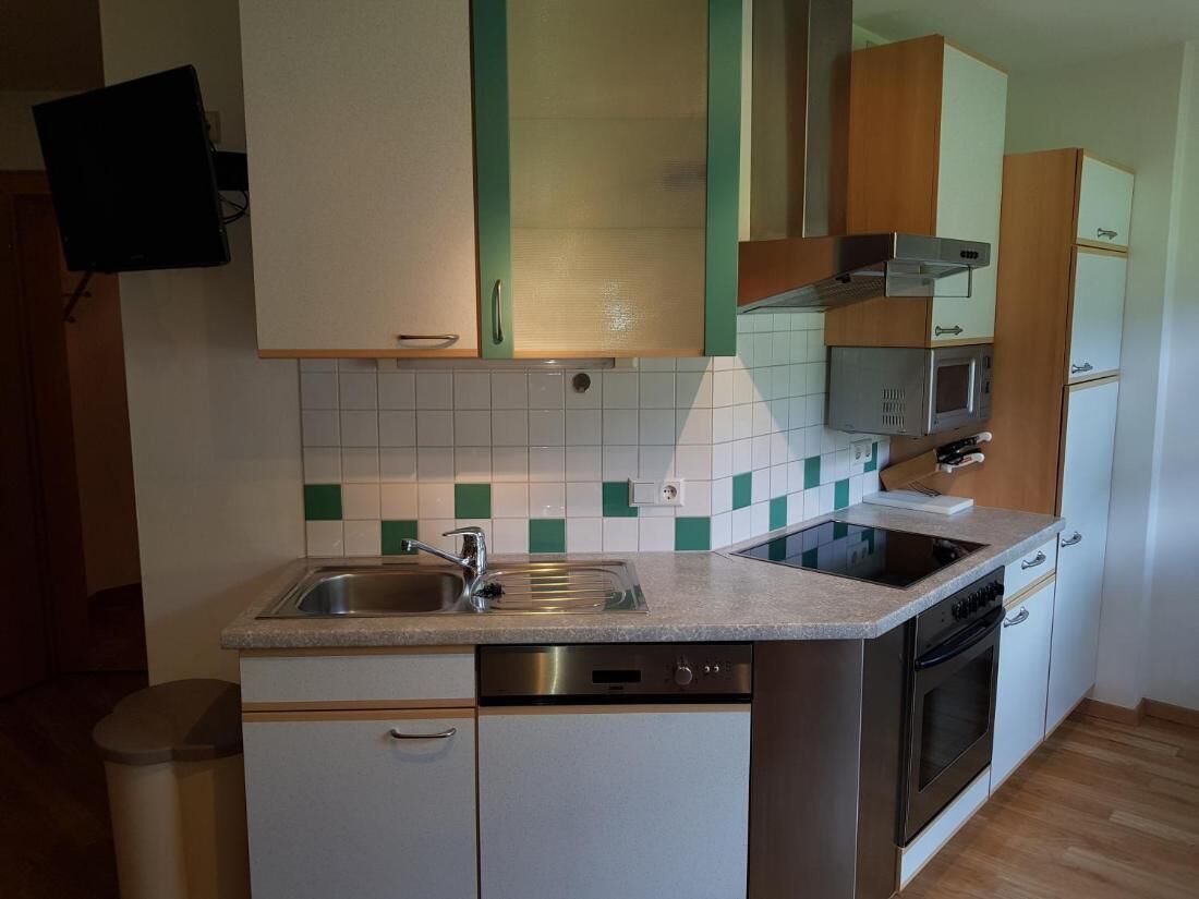 A compact kitchen with a dishwasher, oven, microwave, and a tiled backsplash.