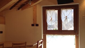 Quarto com mesa de jantar e cadeiras de madeira, janela com vidro jateado e teto com vigas aparentes.