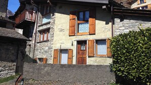 Um edifício de pedra tradicional com venezianas de madeira, varanda e chaminé.