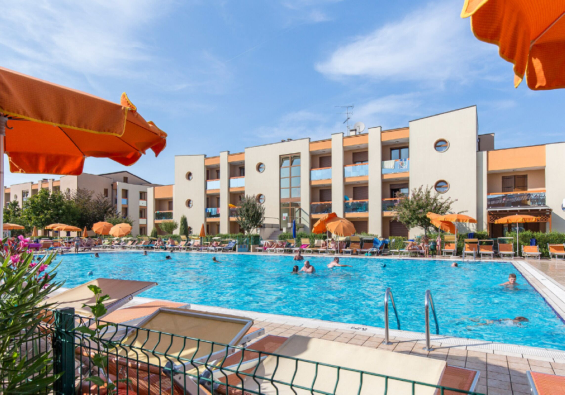 A swimming pool with lounge chairs and umbrellas, surrounded by a building with multiple balconies.