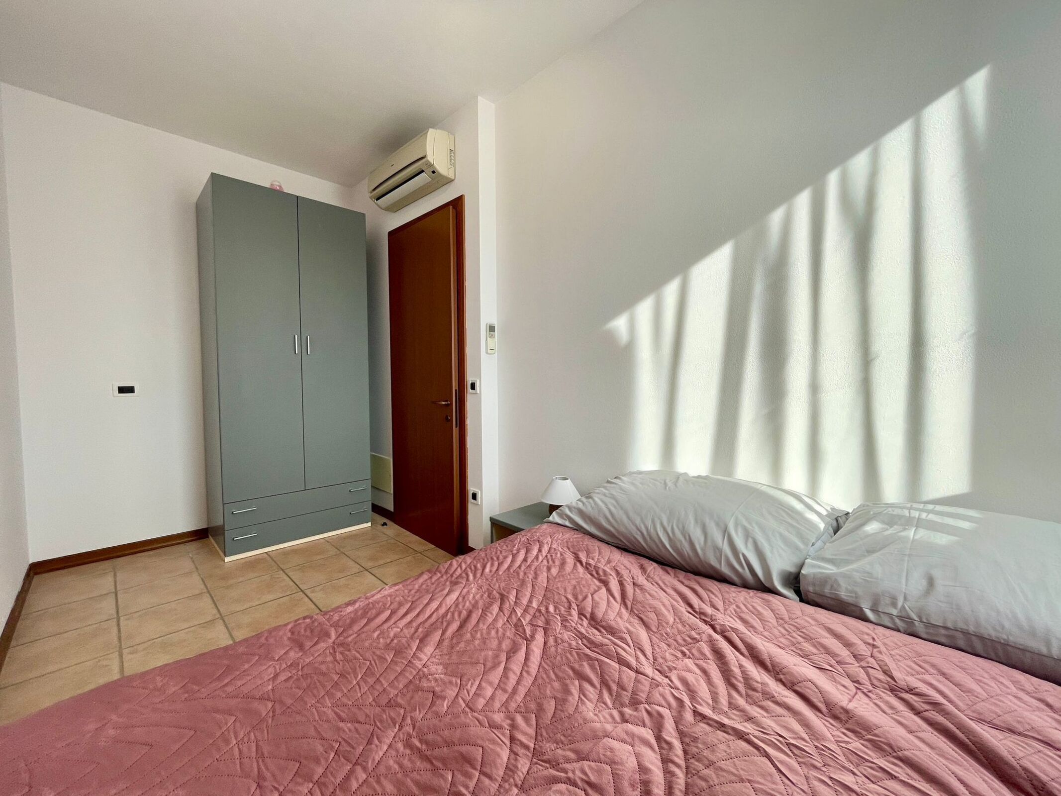 A bedroom with a bed, a wardrobe, a door, and an air conditioning unit.