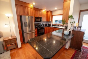 A modern kitchen with wooden cabinets, stainless steel appliances, a granite countertop, and a potted plant.