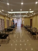 A hotel dining area with multiple tables and chairs, ceiling fans, and recessed lighting.
