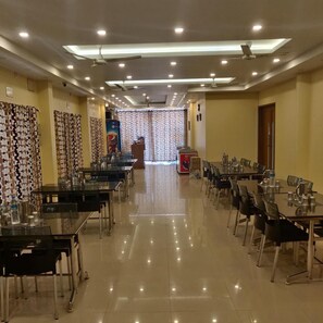 A hotel dining area with multiple tables and chairs, ceiling fans, and recessed lighting.