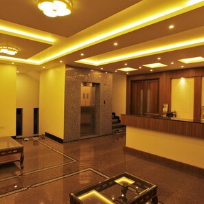 A hotel lobby with a reception desk, a glass coffee table, a reception area, and a staircase.