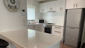 A modern kitchen with white cabinetry, a stainless steel refrigerator, a microwave, and a gas stove. - Momiji Brooklyn (Furano)
