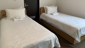 Two single beds with white linens and pillows, a black door, and a small light switch on the wall. - Momiji Brooklyn (Furano)