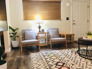 Une pièce comprenant deux fauteuils gris, une table d’appoint en bois, un tapis à motifs et une plante en pot.
