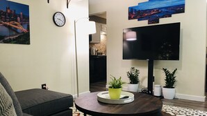 Un salon moderne avec un téléviseur à écran plat, une table basse ronde, des canapés gris et un tapis à motifs.