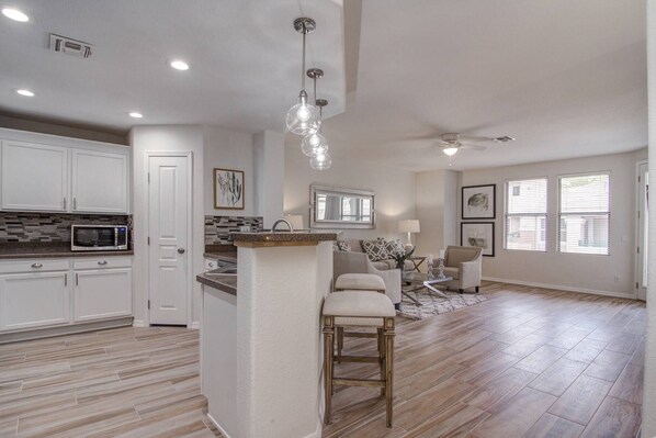 A spacious kitchen with white cabinets, a microwave, and a large island with a bar stool. - Great Location! Dining, Shopping, FREE GOLF, Hiking, Heated Pool, Spa & Fitness Room, Garage + WIFI (Scottsdale)