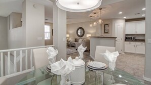 Een eethoek met een glazen tafel, gedekt voor zes personen, witte servetten en een decoratief middelpunt.