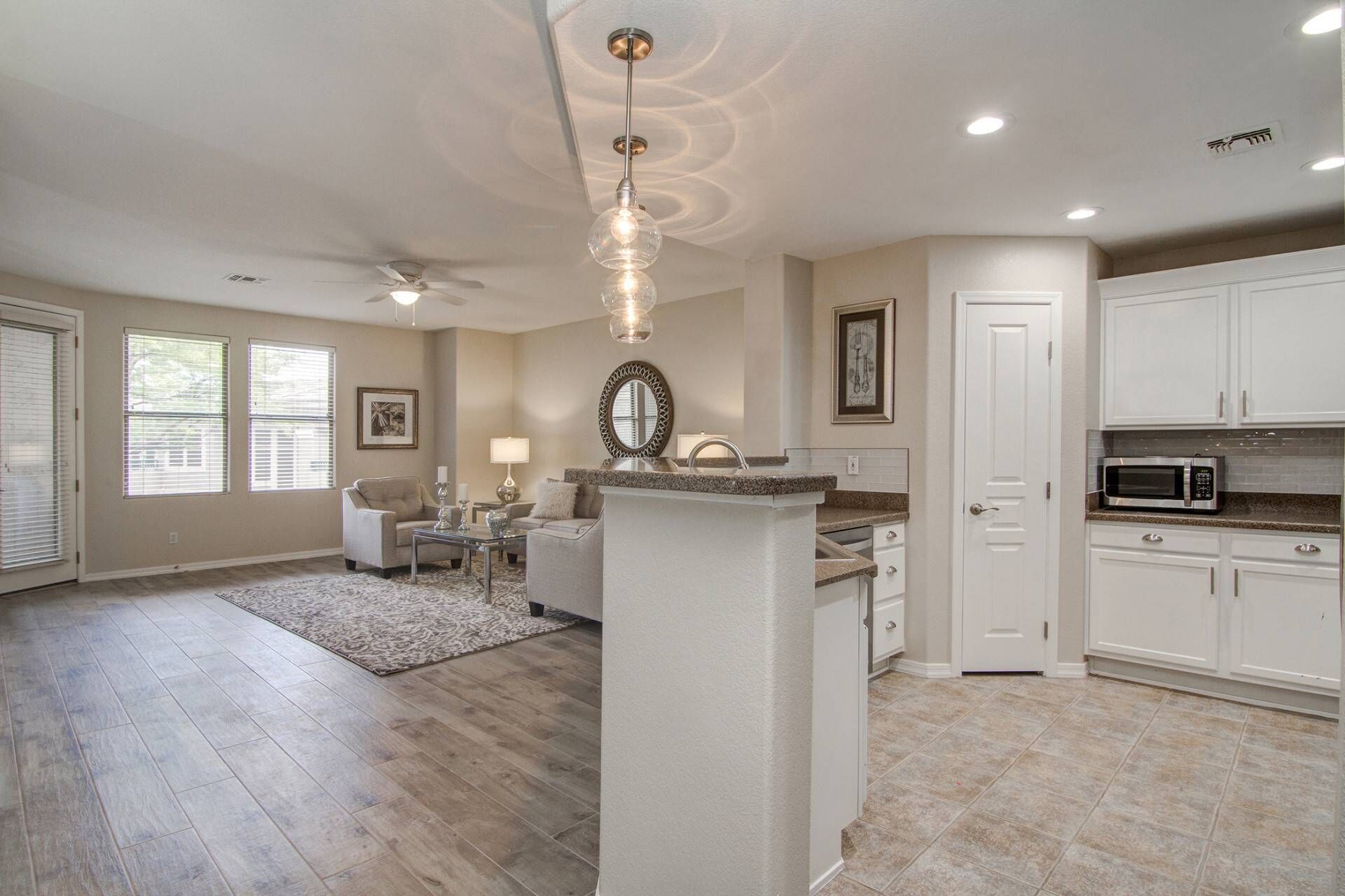 A spacious living room with a ceiling fan, a fireplace, and a kitchen area with white cabinets and a microwave.