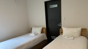 Two single beds with white linens and pillows, a black door with a small window, and a light switch on the wall. - Momiji Montana (Furano)