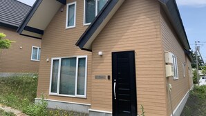 A modern two-story house with a sloped roof, large windows, and a black front door. - Momiji Montana (Furano)