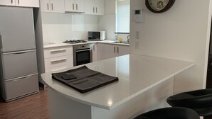 A modern kitchen with white cabinets, a built-in oven, a microwave, and a large island with a leather mat. - Momiji Montana (Furano)
